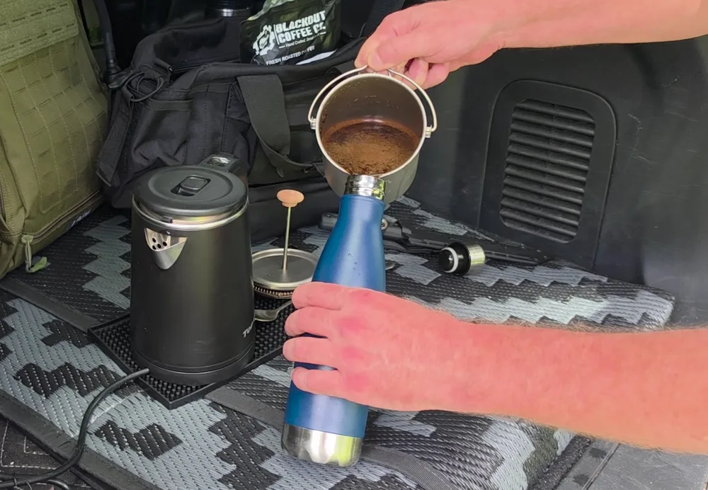 Fresh coffee being poured from a metal brewer into a blue insulated bottle in the SUV.