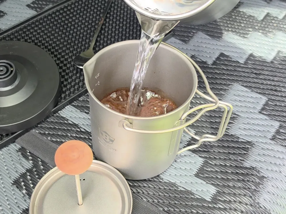 Hot water pouring into coffee in a metal road-trip brewer.